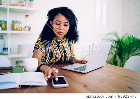 Thoughtful woman using smartphone and laptop at home 65922478