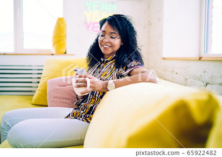 Cheerful young woman drinking coffee browsing smartphone Cheerful young woman drinking coffee browsing smartphone 65922482