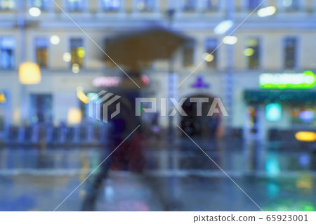 Abstract blurred background of hurrying person, under umbrella, city street in rainy evening, bokeh of the illuminated city 65923001