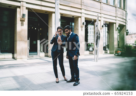 Concentrated colleagues surfing cellphone in street 65924153