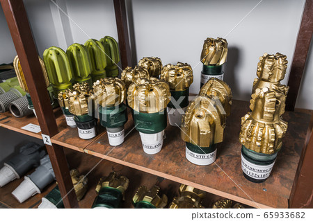 Golden color rock Drill Bits on shelving in stock. Oil drilling equipment for drilling rig operation on oil platform in oil and gas industry. Brand new PDC Polycrystalline Diamond Compact drilling bit 65933682