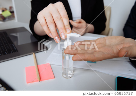 Close-up of hands using antiseptic gel to disinfect hands over a work desk in an office. Preventive measures during the period of epidemic and social exclusion. Close-up of hands using antiseptic gel to disinfect hands over a work desk in an office. Preventive measures during the period of epidemic and social exclusion. 65935737