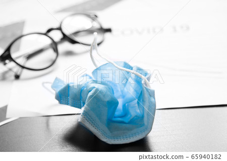 End of pandemic coronavirus and isolation. Used crumpled medical mask against glasses and chart for reducing the incidence of morbidity and mortality. End of pandemic coronavirus and isolation. Used crumpled medical mask against glasses and chart for reducing the incidence of morbidity and mortality. 65940182