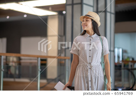 Brunette female in straw hat standing with tickets and suitcase, smiling Brunette female in straw hat standing with tickets and suitcase, smiling 65941769
