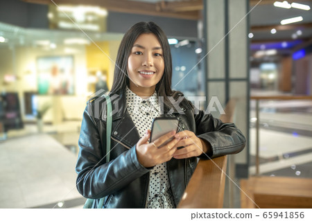 Young brunette female leaning on stair rails, holding her smartphone, smiling Young brunette female leaning on stair rails, holding her smartphone, smiling 65941856