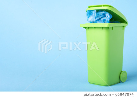 green trash can with polyethylene waste on a blue background with place for text green trash can with polyethylene waste on a blue background with place for text 65947074