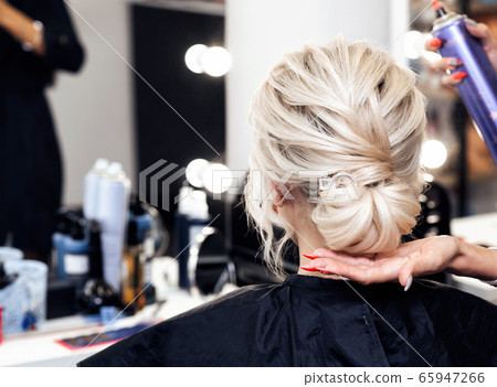 hairdresser makes his own hands hairstyle a bun on the head of a blonde girl 65947266