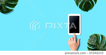 Person using a tablet computer with tropical leaves Person using a tablet computer with tropical leaves 65948243