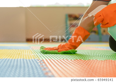Woman hand in protective orange rubber gloves holding green microfiber cleaning cloth and wiping dust using a spray sterilizing solution make cleaning and disinfection for good hygiene 65949141