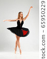 Girl in a black ballet dress. Ballerina in a dark ballet tutu on a light background. The young ballerina is warming up 65950229