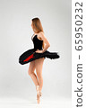 Girl in a black ballet dress. Ballerina in a dark ballet tutu on a light background. The young ballerina is warming up 65950232