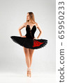 Girl in a black ballet dress. Ballerina in a dark ballet tutu on a light background. The young ballerina is warming up 65950233