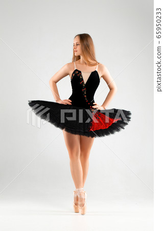 Girl in a black ballet dress. Ballerina in a dark ballet tutu on a light background. The young ballerina is warming up Girl in a black ballet dress. Ballerina in a dark ballet tutu on a light background. The young ballerina is warming up 65950233