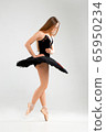 Girl in a black ballet dress. Ballerina in a dark ballet tutu on a light background. The young ballerina is warming up 65950234