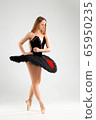 Girl in a black ballet dress. Ballerina in a dark ballet tutu on a light background. The young ballerina is warming up 65950235
