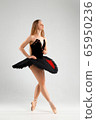 Girl in a black ballet dress. Ballerina in a dark ballet tutu on a light background. The young ballerina is warming up 65950236