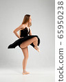 Girl in a black ballet dress. Ballerina in a dark ballet tutu on a light background. The young ballerina is warming up 65950238