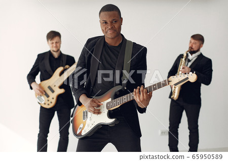 Black man in black suit standing with a guitar 65950589