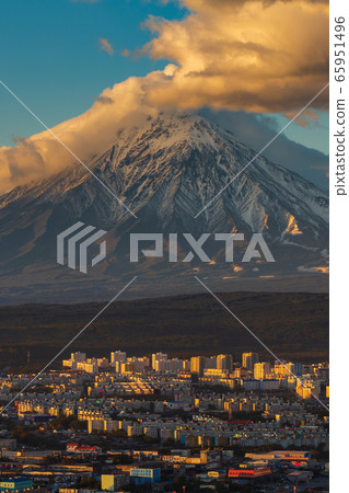 Evening view from above of Petropavlovsk-Kamchatsky City at sunset on background active volcano of Kamchatka Peninsula. Evening view from above of Petropavlovsk-Kamchatsky City at sunset on background active volcano of Kamchatka Peninsula. 65951496
