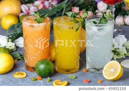 Summer fresh cold drink beverages. Ice Lemonade in the jug and lemons and orange with mint on the table outdoor. Orange lemonade in a glass. 65952150