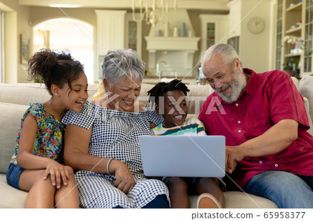 Senior mixed race couple sitting on the couch with their young grandson and granddaughter Senior mixed race couple sitting on the couch with their young grandson and granddaughter 65958377