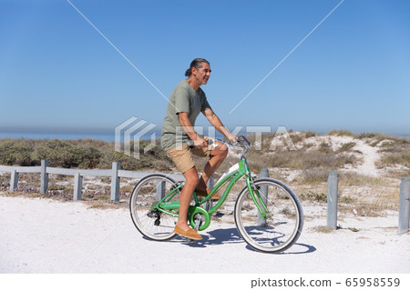 Senior Caucasian man riding a bike at the beach 65958559