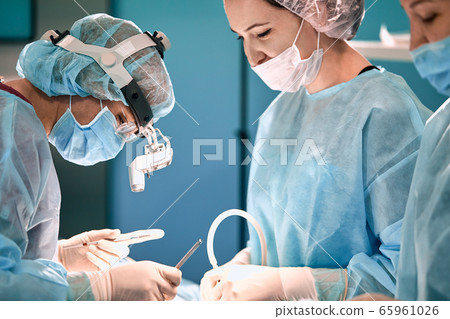 Modern surgery in a technologically advanced hospital. Bright room of intensive care. Doctors and assistants working in the operating room save lives. Modern surgery in a technologically advanced hospital. Bright room of intensive care. Doctors and assistants working in the operating room save lives. 65961026