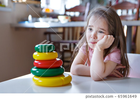 child is bored while collecting tpyramid details of toy, sad face. Concept of fine motor skills development, educational games, childhood,children's day, kindergarten copyspace, bad mood, house arrest 65961649