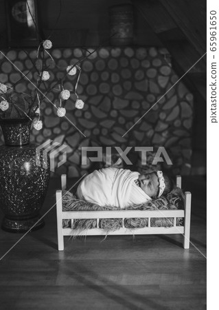 baby is lying in wooden bed under blanket against background of stacked firewood and decorative vase. portrait of small child. concept of childhood, health, IVF, children's furniture, interior 65961650