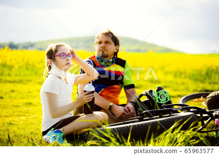 Sport and quarantine. 9 years girl ciclist with father having rest breathing without masks admist the fields in the sunny day 65963577