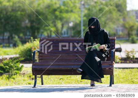 Muslim woman is reading a book on a bench. Muslim woman is reading a book on a bench. 65968909