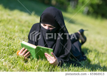 Islamic woman reads a book on a lawn in a park. Islamic woman reads a book on a lawn in a park. 65968913