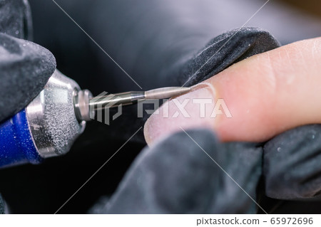 Hardware manicure in a beauty salon. Female manicurist is applying electric nail file drill to manicure on female fingers. Mechanical manicure close-up. Concept body care. Hardware manicure in a beauty salon. Female manicurist is applying electric nail file drill to manicure on female fingers. Mechanical manicure close-up. Concept body care. 65972696