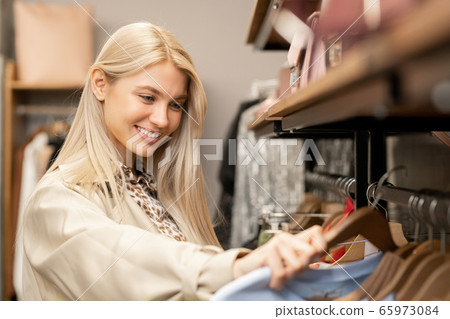 Smiling young blond woman with long hair looking through new fashion collection 65973084