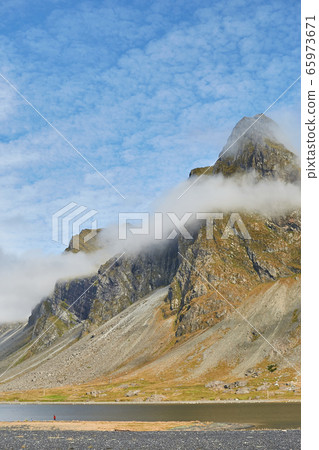 Foggy mood. Amazing shot of impressive Eystrahorn mountain chain in Iceland with fog rings around, blue sky on the background Foggy mood. Amazing shot of impressive Eystrahorn mountain chain in Iceland with fog rings around, blue sky on the background 65973671