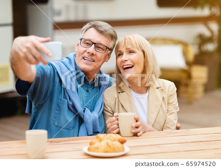 Camping season. Cheerful mature couple taking selfie while having breakfast near motorhome outside 65974520