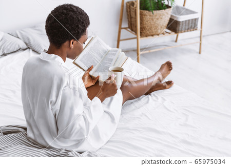 Reading in bed. African american woman in white coat with book in bedroom 65975034