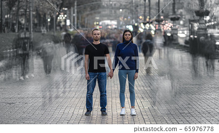 The man and woman stand on the crowded street and hold hands 65976778