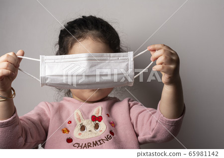 Little girl trying to wear a mask for protection Little girl trying to wear a mask for protection 65981142