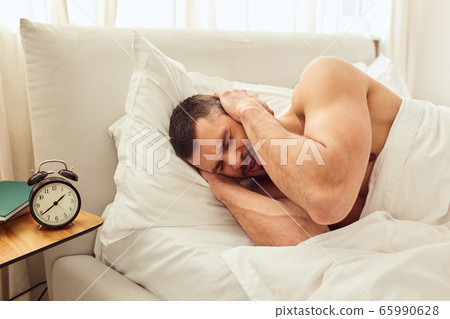 Displeased gentleman covering ears while alarm clock ringing Displeased gentleman covering ears while alarm clock ringing 65990628