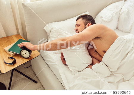 Handsome young man turning off alarm clock Handsome young man turning off alarm clock 65990645