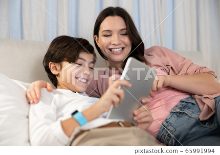 Boy with a gadget sitting next to his mother 65991994