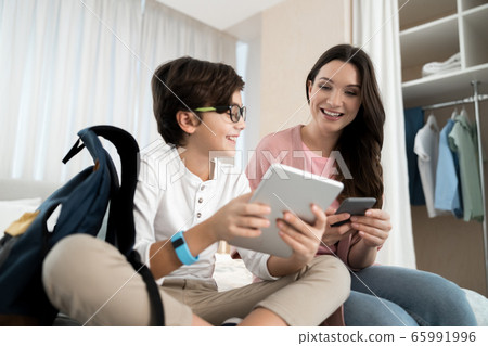 Woman with a smartphone staring at her son tablet 65991996