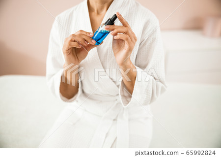 Female in bathrobe holding serum for face treatment Female in bathrobe holding serum for face treatment 65992824