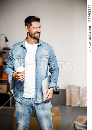 Happy young man with laptop and hot drink in new flat 65993322
