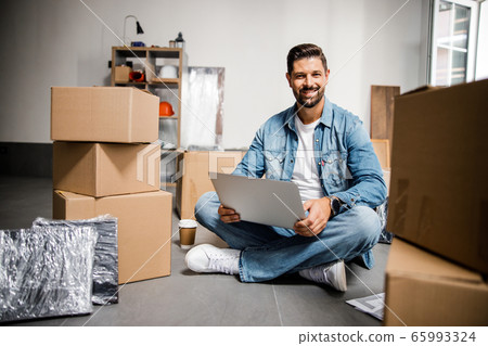 Happy male with laptop relaxing after moving to new flat 65993324