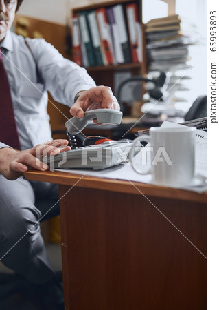 Male employee putting down the receiver of an old-fashioned phone Male employee putting down the receiver of an old-fashioned phone 65993893