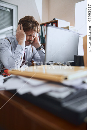 Mature businessman going through stress situation at his working desk Mature businessman going through stress situation at his working desk 65993917