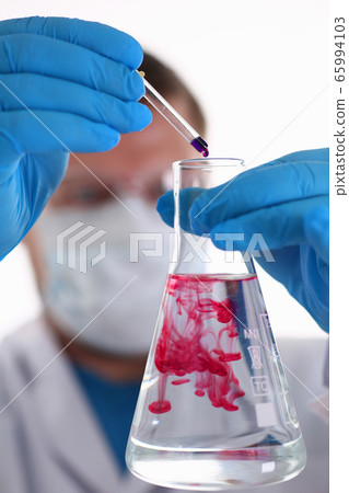 A male chemist holds test tube of glass in his hand overflows a liquid A male chemist holds test tube of glass in his hand overflows a liquid 65994103