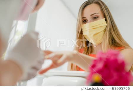 Woman with face mask during manicure in nail salon Woman with face mask during manicure in nail salon 65995706